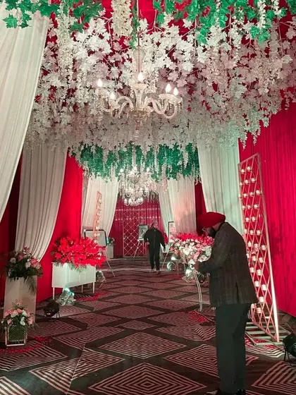 A festive red and white themed entrance. The ceiling is decorated with hanging white wisteria flowers and chandeliers, creating a beautiful contrast with the red draped walls.