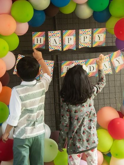 Teamwork makes the dream work. Kids helping to set up the 'Happy Birthday' banner is a sweet, candid moment from the party preparations.