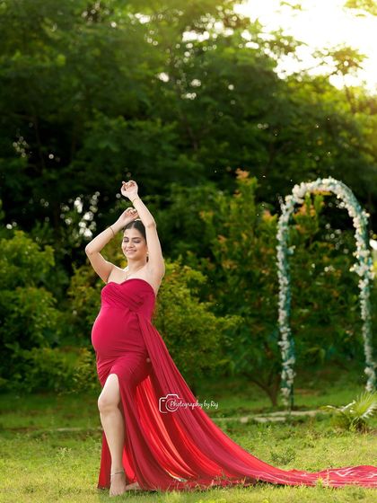 A graceful pose in a flowing red fabric wrap. The golden hour lighting in our garden creates a magical, warm glow around the mother-to-be.
