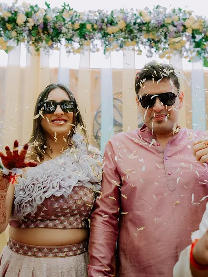 A fun-filled moment from a Haldi ceremony, with the couple wearing sunglasses and being showered with flower petals. We capture the playful side of wedding rituals.