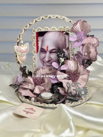 A delicate and shimmering Guruji Darbar with metallic pink and purple flowers on a mirrored base. The design includes a pearl-studded frame and a hanging heart charm, adding a touch of elegance.