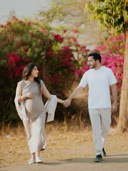 A full-length shot of an expecting couple walking hand-in-hand. The vibrant flowers in the background add a pop of color to this romantic outdoor maternity session.