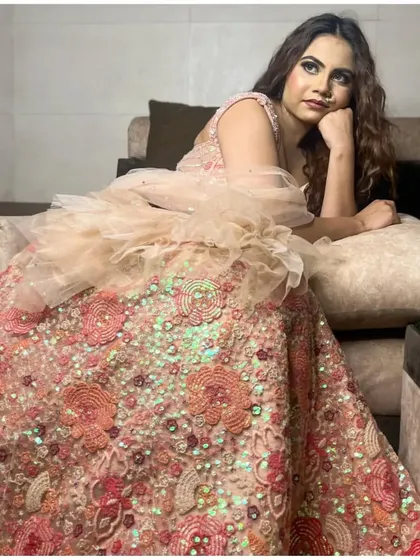 A relaxed, candid-style shot of the client on a sofa in the peach lehenga.