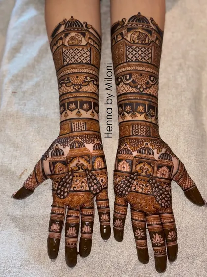This full-coverage bridal mehendi is filled with architectural details, from domes on the arms to intricate windows on the palms. The design uses negative space to make the patterns pop.