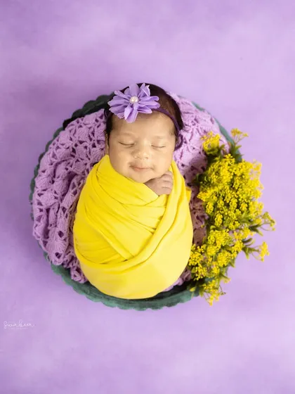 A pop of color can bring such joy to a newborn portrait. Here, a bright yellow swaddle contrasts beautifully with a soft lavender background, showing how we can play with different palettes to match your style.