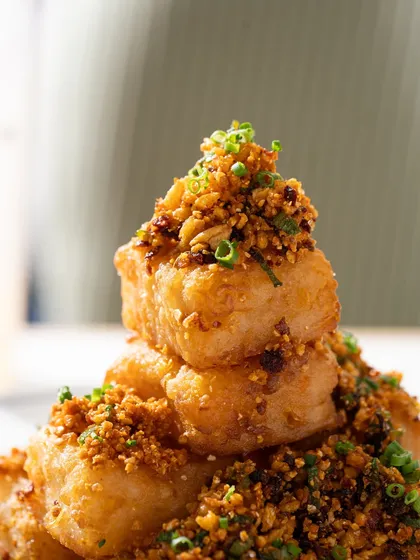 A stack of crispy fried turnip cakes. The close-up angle emphasizes the crunchy texture and savory topping.