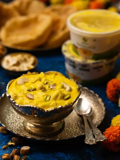 A festive shot of Shrikhand Puri for Gudi Padwa. The vibrant yellow of the shrikhand against the deep blue background creates a visually stunning contrast.