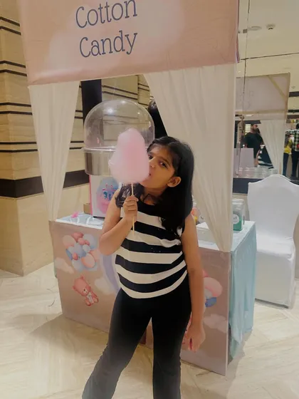 Posing with a perfectly pink puff of cotton candy. Our themed stalls, like this pastel 'Cotton Candy' setup, add a beautiful touch to any party's aesthetic.