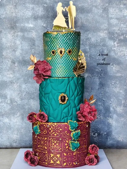 For this grand wedding celebration, I designed a three-tiered cake with rich jewel tones. Each tier features a different non-fondant texture, from a quilted pattern to geometric embossing and a gold-stenciled base, all brought together with deep red sugar flowers.