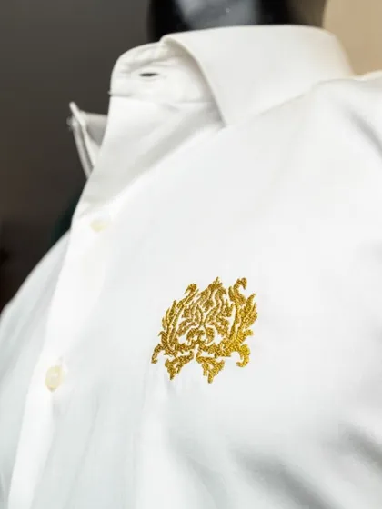 We can add custom embroidery to our shirts, like this intricate gold logo. This level of personalization is perfect for corporate branding or adding a unique monogram to a gift.