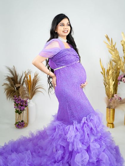A beautiful lavender lace gown with a dramatic ruffled train. This side profile shot beautifully accentuates the baby bump, set against our bright studio background with pampas grass decor.