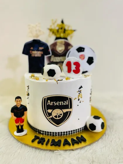 An Arsenal FC themed cake for a 13th birthday. The design includes the team logo, a jersey, and multiple footballs for a true fan.