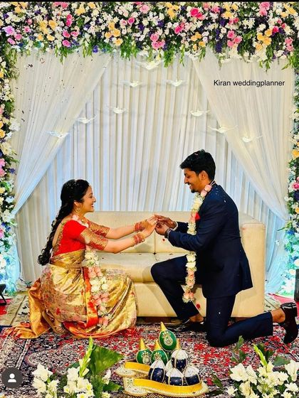 A picture-perfect proposal moment during an engagement ceremony, set against a backdrop of a floral arch and white drapes.