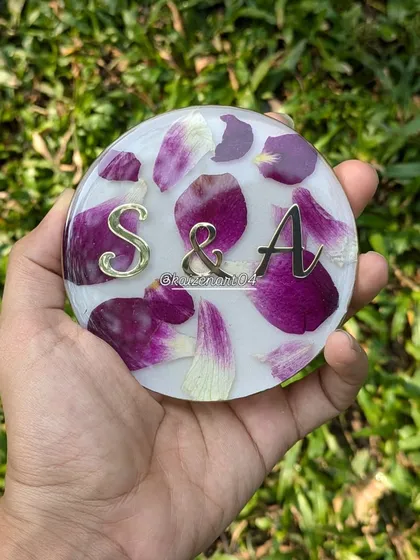 A 4-inch circular keepsake with purple petals and the couple's initials. The gold lettering and border add a touch of luxury to this small but meaningful piece.