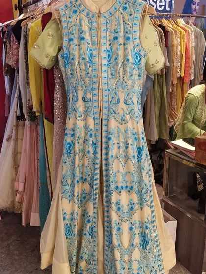 An elegant cream-colored Anarkali with a contrasting open-front jacket featuring bold blue floral embroidery. This is a sophisticated and unique piece for a discerning fashion lover.