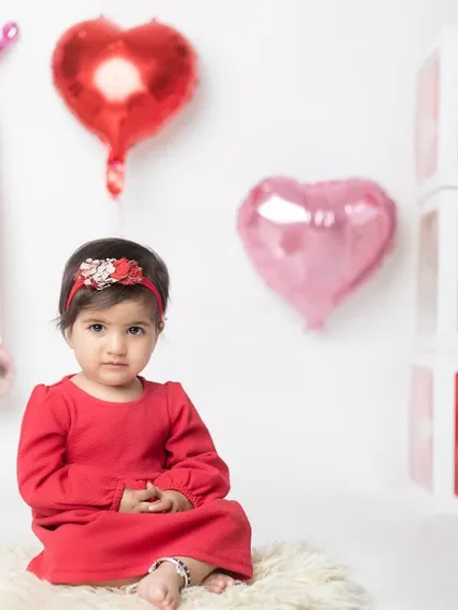 A simple and classic first birthday setup with red and pink heart balloons and 'ONE' blocks. The focus is all on her sweet face.