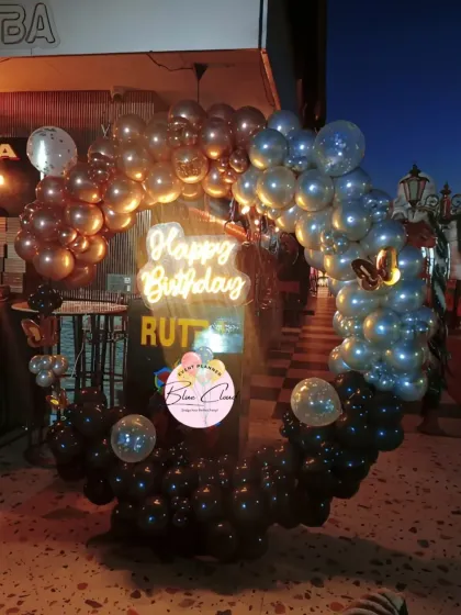 An outdoor birthday setup with a balloon arch in black, rose gold, and silver tones.