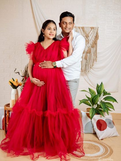 A beautiful indoor maternity portrait with a partner. The striking red of the gown makes the expecting mother the center of attention, while the soft tulle ensures a comfortable fit.