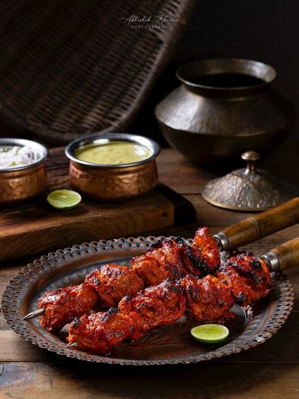 Chicken Gulnaar tikka on skewers, styled with traditional copper bowls and dips for The Nawaab's. The image is composed to look like a classic appetizer serving.