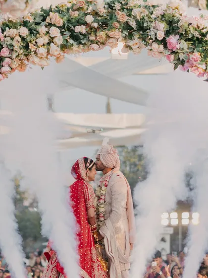 A tender moment under a floral arch, enveloped in a cloud of smoke. I use special effects to enhance the romance and create ethereal photo opportunities during key moments like the Varmala.