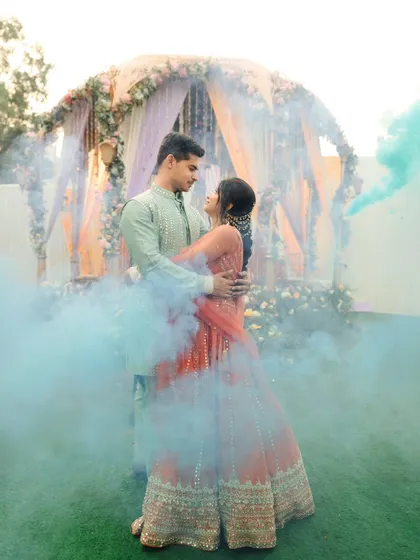 A romantic portrait of the couple surrounded by blue smoke bombs during their Haldi event. It adds a touch of modern drama to the traditional ceremony.