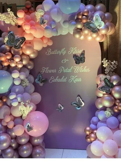 A personalized butterfly-themed backdrop with custom text, surrounded by a stunning balloon arch in shades of purple, pink, and rose gold.