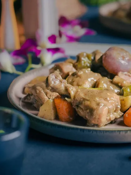A close-up of the Dumphukt Rosh Chicken, highlighting the tender chicken drumstick and the wholesome vegetables in the creamy sauce.