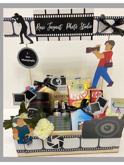 A hamper designed for the photography lover in your life. This creative gift is decorated with film strips and camera cutouts, and includes a camera lens-shaped mug and other themed goodies.