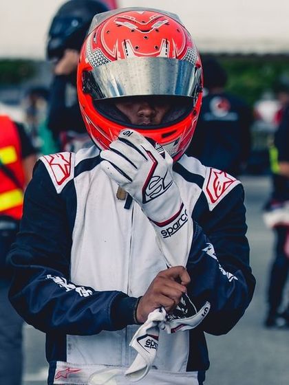 A driver prepares for the start of the RMC Asia Max race, adjusting his gloves with intense focus amidst the crowd of competitors.