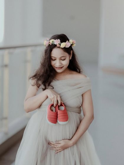 A close-up maternity photo focusing on the mother-to-be, who is holding a tiny pair of red baby shoes near her belly. This symbolic portrait is full of anticipation and love for the coming baby.