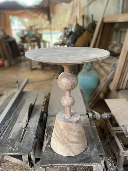 A turned-wood side table on a conical base, shown in the workshop.