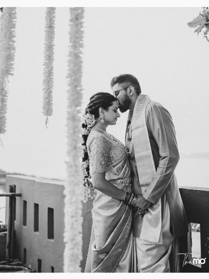 A timeless black and white portrait. The groom's gentle kiss on the bride's forehead speaks volumes, capturing a moment of tenderness and protection against a soft, beautiful backdrop.