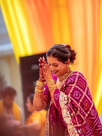 The bride smiling with her hands in a respectful 'namaste' pose, showing a moment of gratitude and happiness during her Haldi.