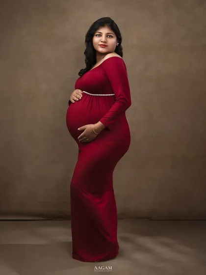 This side profile in a simple red gown against a solid backdrop emphasizes the beautiful silhouette of pregnancy.