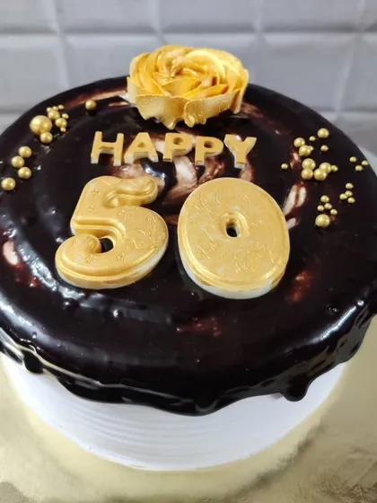 A rich chocolate cake celebrating a 50th milestone. The golden numbers and rosette add a touch of elegance.