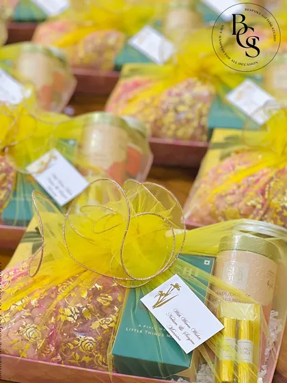 A festive hamper wrapped in bright yellow organza. The sheer fabric allows the contents to be partially visible, building anticipation, while the gold-edged ribbon adds a touch of celebratory sparkle.