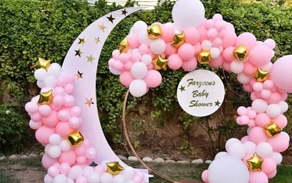 A 'Twinkle Twinkle Little Star' baby shower theme with a crescent moon prop and a circular balloon arch in pink, white, and gold.