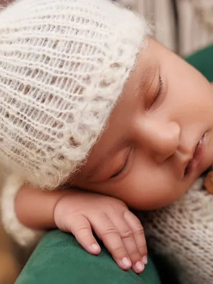 A close-up portrait of a sleeping newborn in a soft, white knit outfit, highlighting their delicate features.