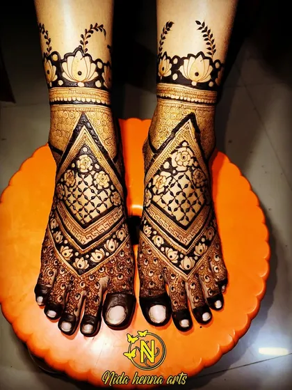 A geometric style bridal feet design with bold, diamond shaped patterns. The dark henna stain creates a striking contrast, making the design stand out.