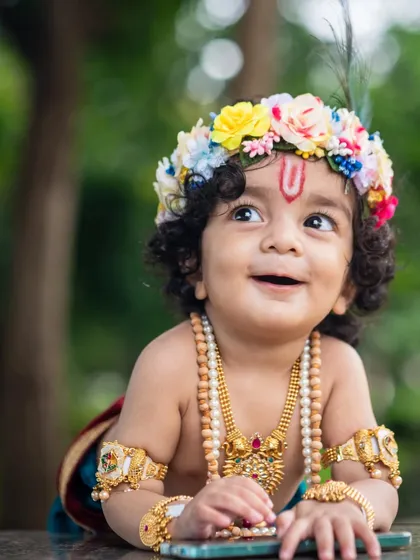 An adorable upward-looking shot of a baby boy dressed as Krishna, with a beautiful, innocent smile.