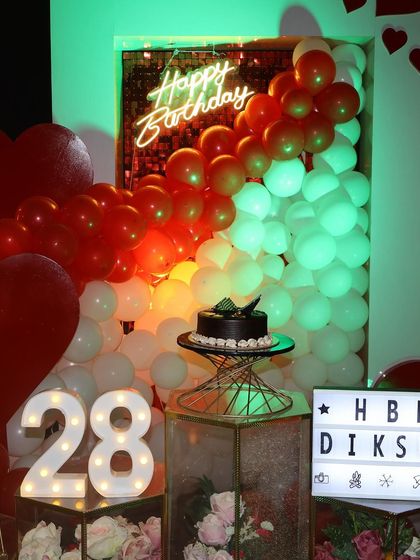 A close-up of the birthday setup, featuring a "Happy Birthday" neon sign, a balloon arch, and the light-up number "28". We pay attention to every detail to make your decor perfect.