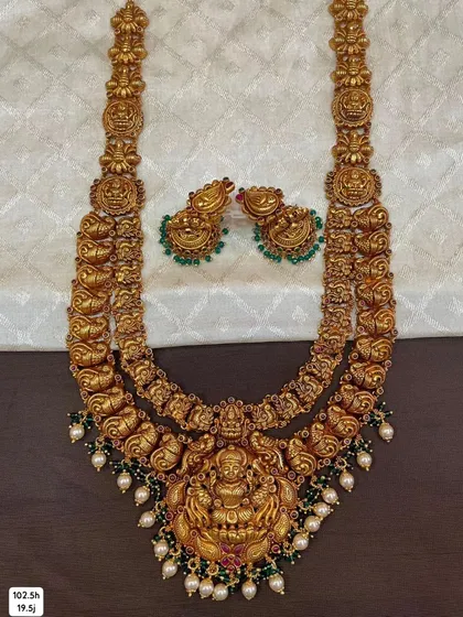 This is a grand two-layer temple haram made from 92.5 silver with gold plating. The necklace features repeating goddess motifs and is finished with green beads and pearls for a divine look.