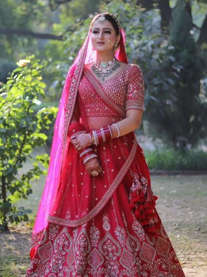 A full-length shot of a bride in a gorgeous red lehenga, set against a natural green background. The look is classic, elegant, and picture-perfect.