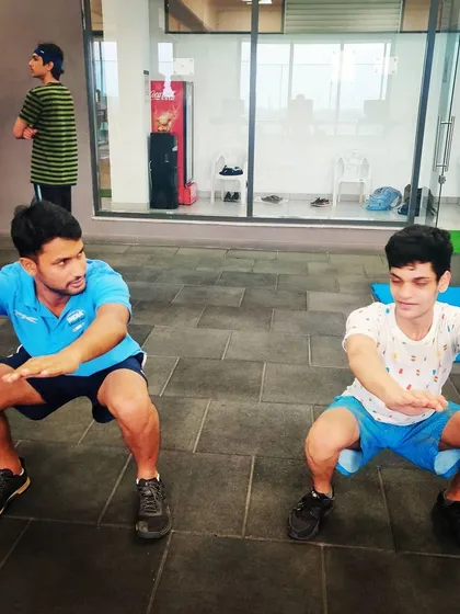 Strength and conditioning are integral to our training. I am seen here doing squats alongside a young athlete, emphasizing the importance of leading by example in physical fitness.