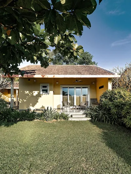 The exterior of a private villa at Dvara Resorts, with its traditional tiled roof and sunny yellow walls, surrounded by a lush private garden. It's the picture of a perfect, peaceful getaway.
