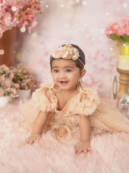 A happy baby girl crawling on a pink fur rug in a beautiful floral setup with disco balls for a touch of sparkle.