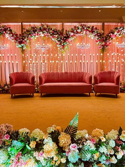 A romantic reception stage with three heart-shaped floral arches, mini chandeliers, and a wall of candle lights, all in a beautiful blush pink theme.