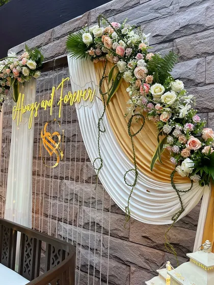 The elegant draping and floral swag on the photo booth backdrop. The combination of white and gold fabrics with fresh flowers creates a look of timeless sophistication.
