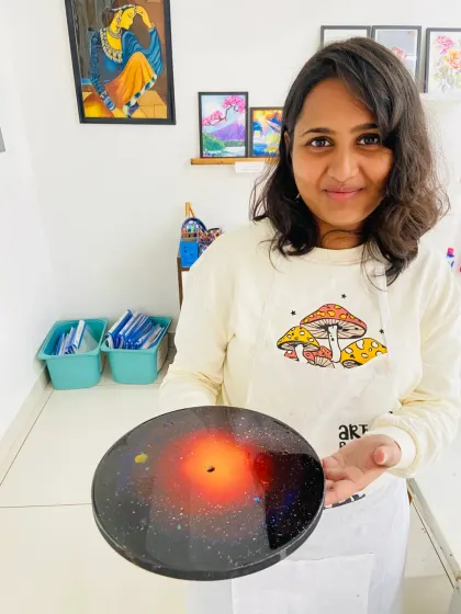 A participant beaming with pride as she holds up the galaxy resin clock she made. In this workshop, you can create your own functional piece of cosmic art to take home.