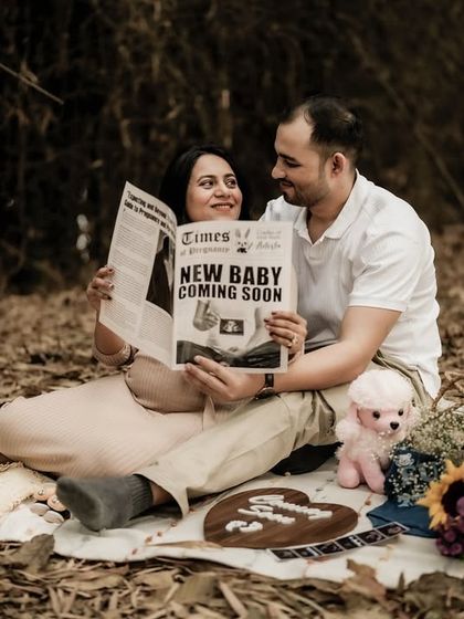 A happy, candid moment of the couple during their picnic announcement. They are reading the "New Baby Coming Soon" newspaper together, sharing a laugh.